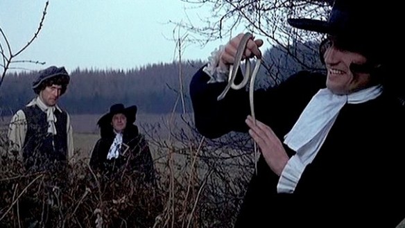 Ralph (Barry Andrews, far left) and The Judge (Patrick Wymark) watch Reverend Fallowfield (Anthony Ainley) toy with a serpent.